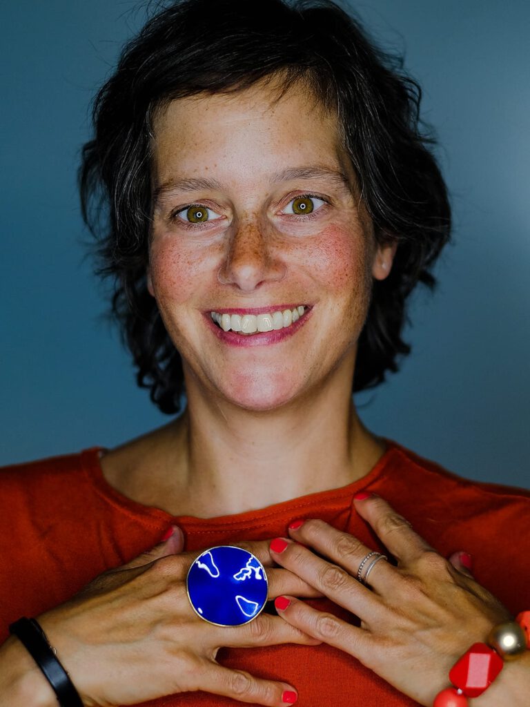 Portrait frontal einer Frau mit dunklen kurzen Haare. ihre Hände auf der Brust abgelegt.