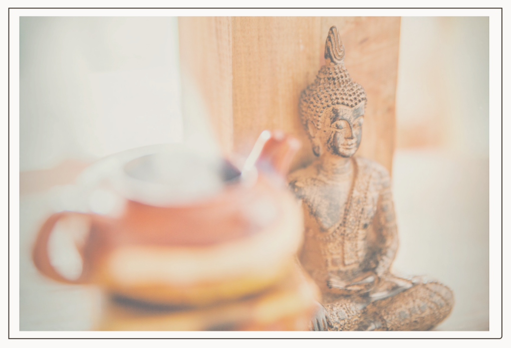 Stillleben, bestehen. aus einer Teekanne im Vordergrund und einer Buddhafigur im Hintergrund, warme, helle Farben, das Bild strahlt Behaglichkeit aus.